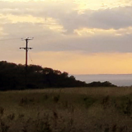 Dark storm clouds out to sea overlaying a bright sunset, viewed from a hillside