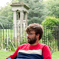 Young man in red and blue sat under a gazebo talking.