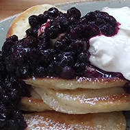 A plate of pancakes with blueberries, syrup and yogurt. Plus a pot of tea.