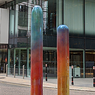 Three coloured shafts eminating from large black stones, outside an office building in central London.