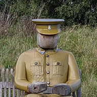 Bench with a life-size wooden figure of a soldier sitting at one end.