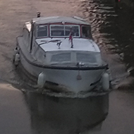 View from a bridge as the sun sets behind clouds facing down river with a boat heading towards you.