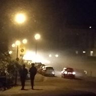 Darkness and fog illuminated by street lamps on a road going uphill away from you