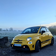 A bright yellow compact city car with black wheels, parked in front of a frost-covered and misty field