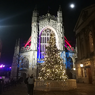 Bath Abbey lit up in blue and red with a lit up Christmas tree in front