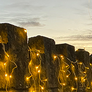 A stone wall alongside a road covered in small lights. The lights give off a warm glow.