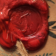 A red wax seal with a letter J stamped onto Christmas wrapping paper