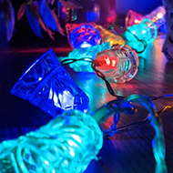 Different coloured Christmas fairy lights, shaped like church bells, laid along a reflective cabinet worktop