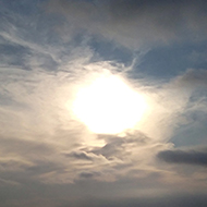 This picture shows the sun going down, slightly obscured by some whispy cloud  and reflected on a calm sea