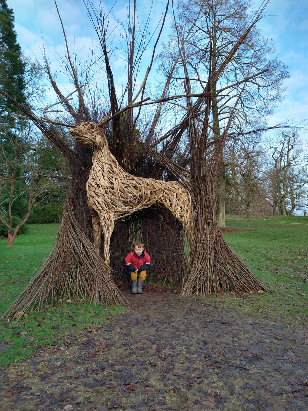 small boy hiding under a wicker deer sculpture