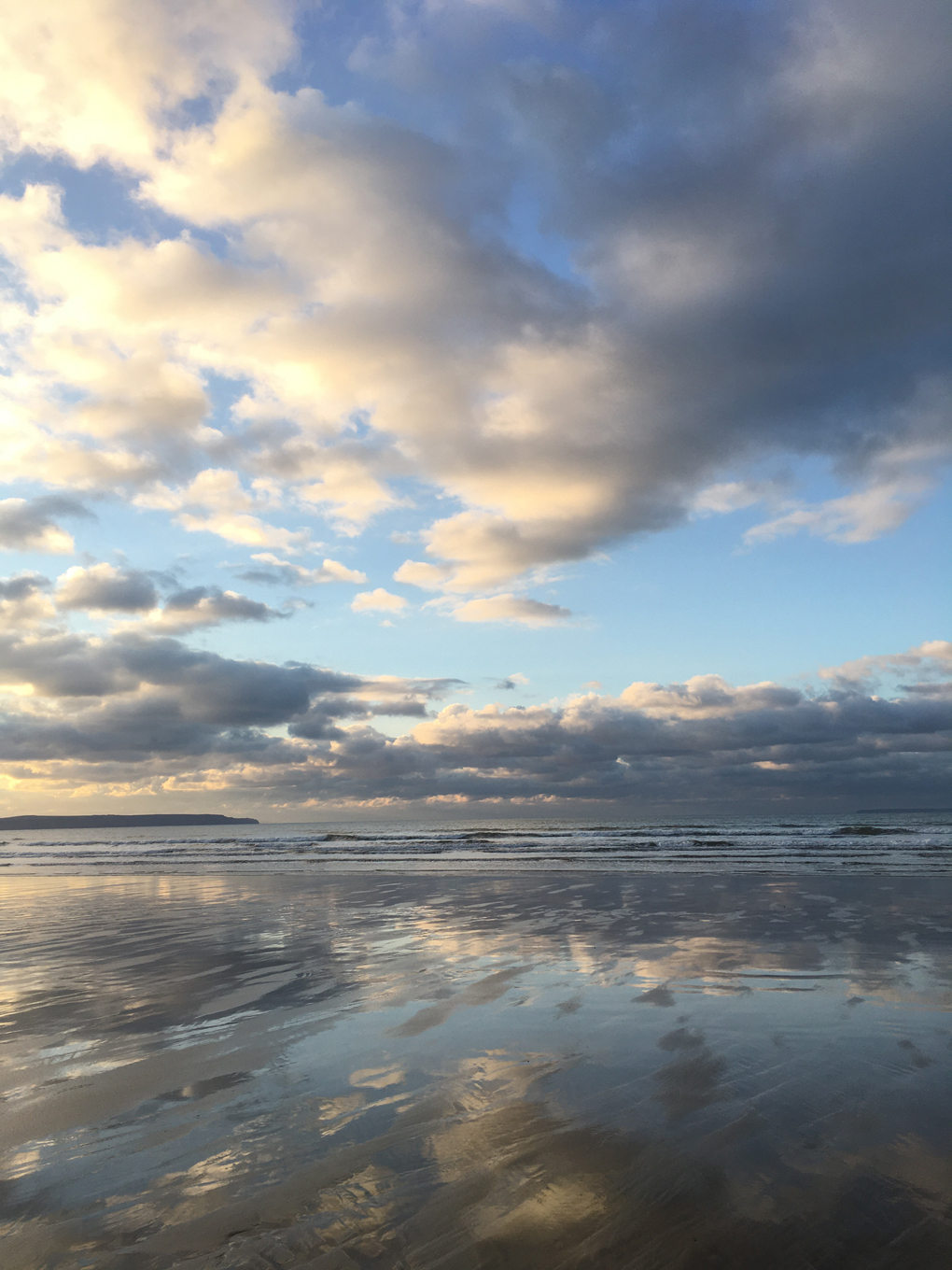 Portrait of clouds reflected in water on Westward Ho! beach at sunset.