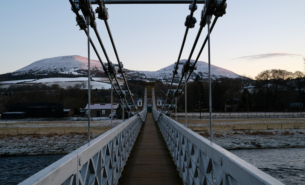 Crossing the Chain Bridge in Melrose, looking towards the Eilon hills with a dusting of snow