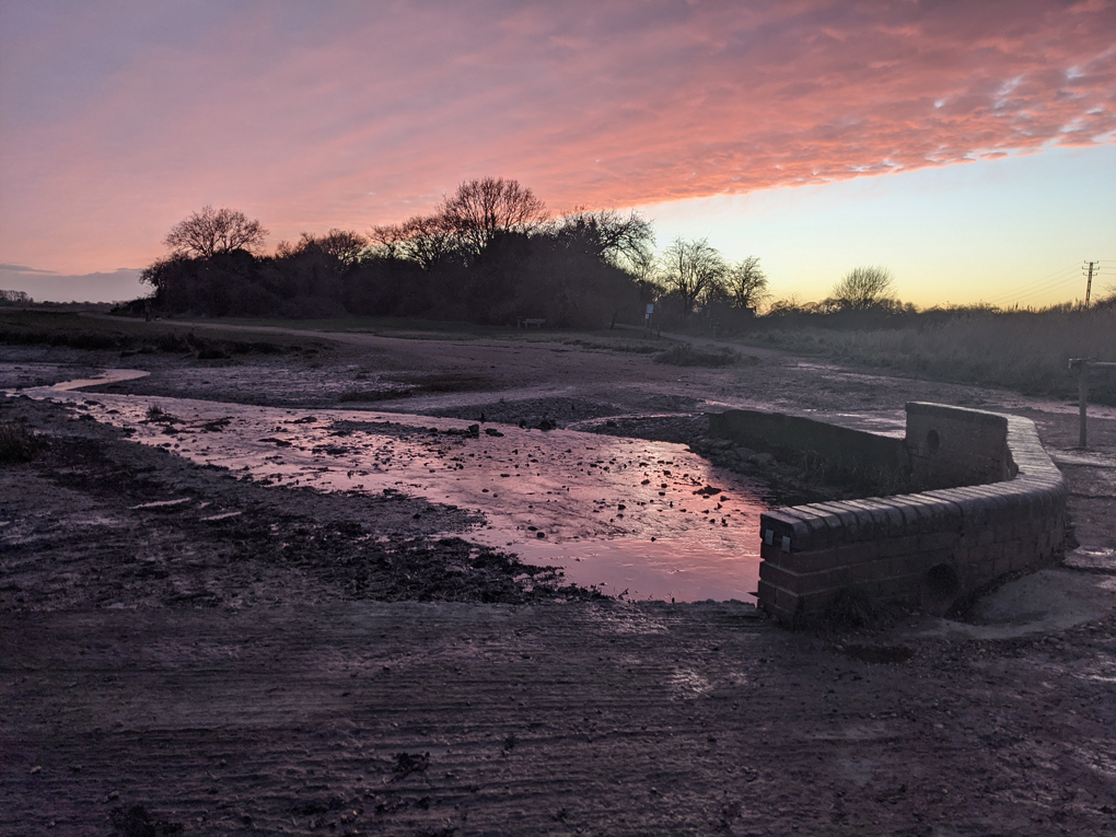 Pink sunset over water, pebbles over beach.