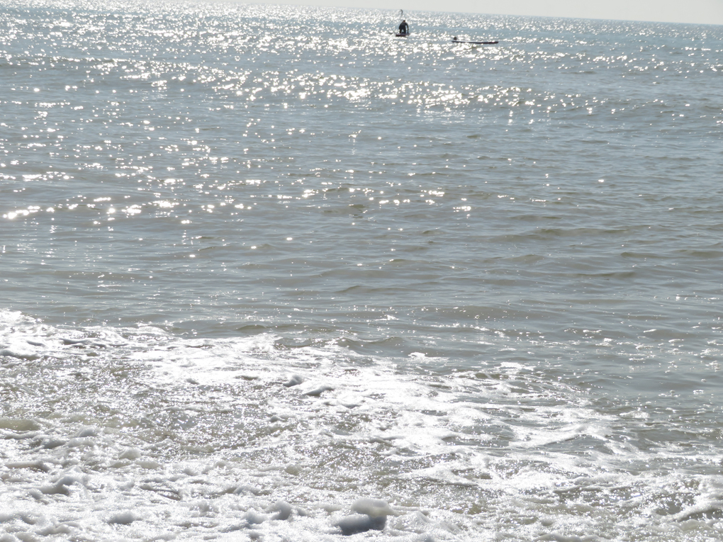 We see sunlight dance on the sea at Goring on Sea with a paddleboarder in the distance
