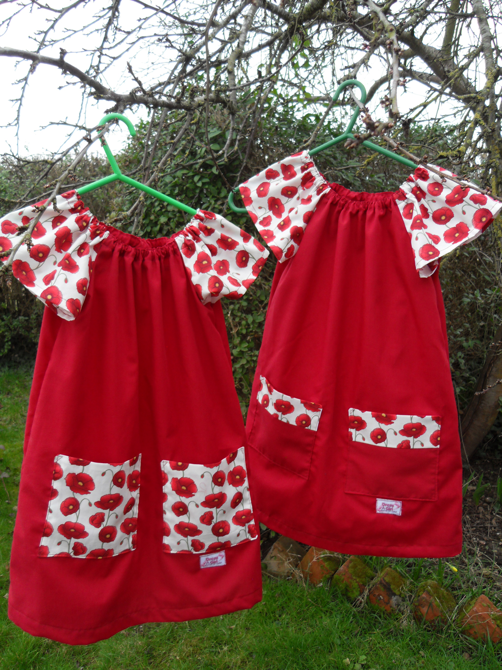 Two red and poppy print girls dresses hanging on tree branches