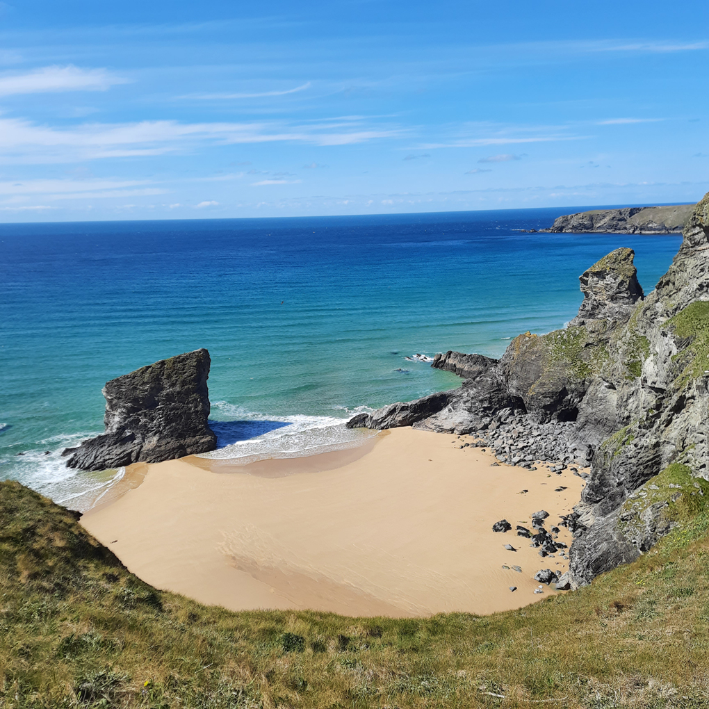Taken from a cliff top, a sandy cove with bright blue waters and yellow sand