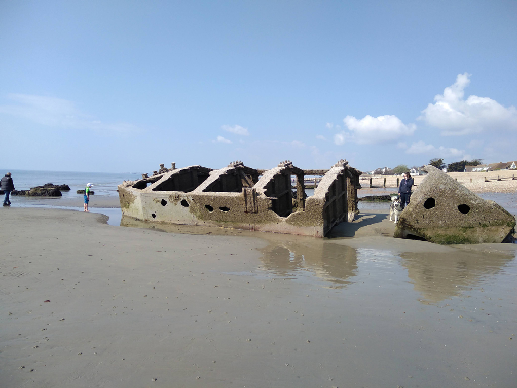 The remains of a concrete  barge lying on its side on a sandy beach