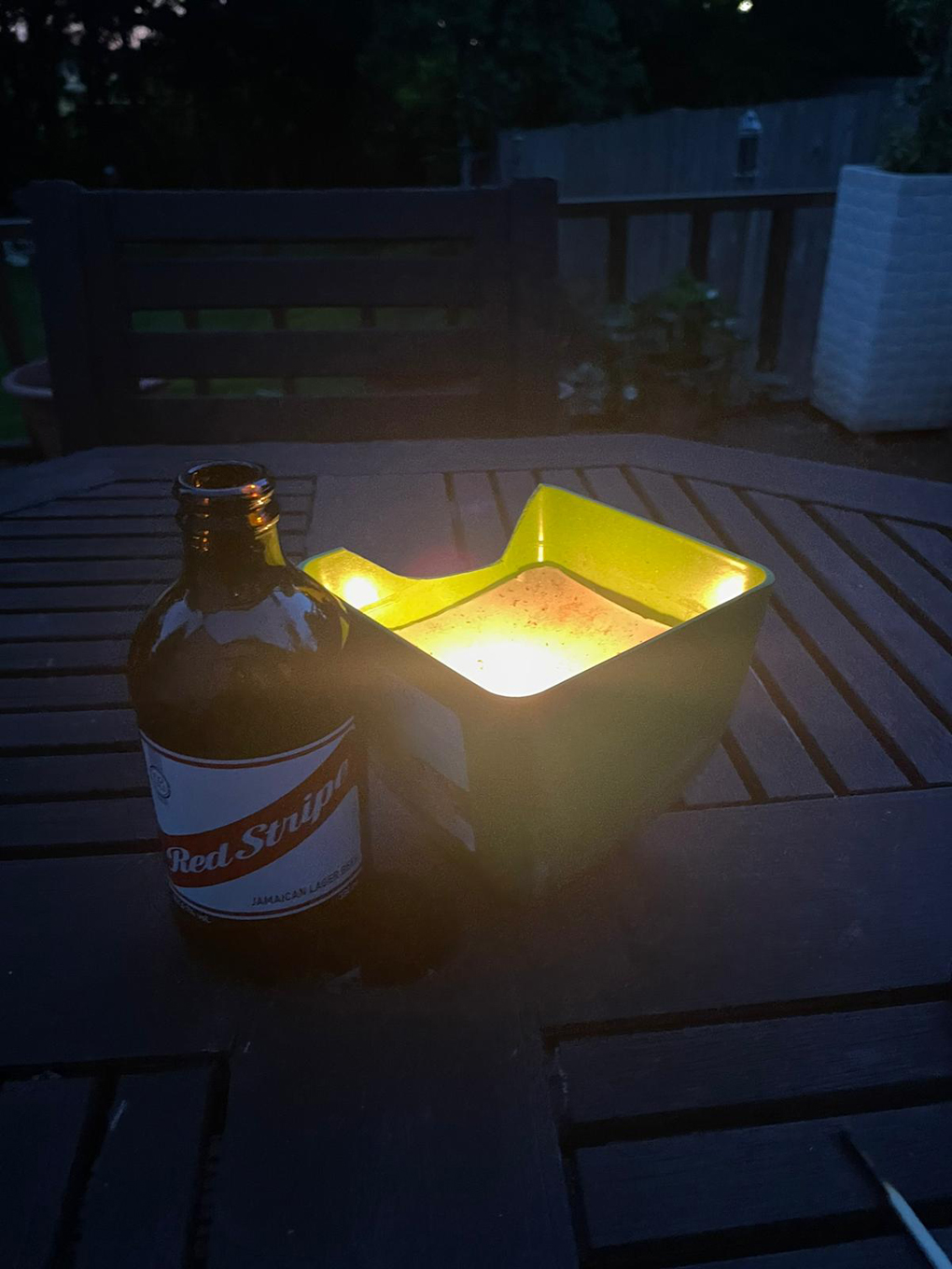 Beer bottle by a lit tea light outside at dusk