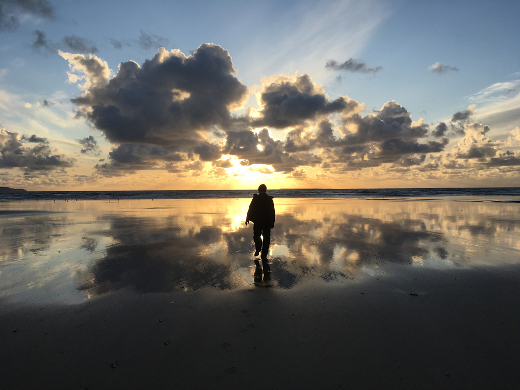Man walking towards sunset on beach