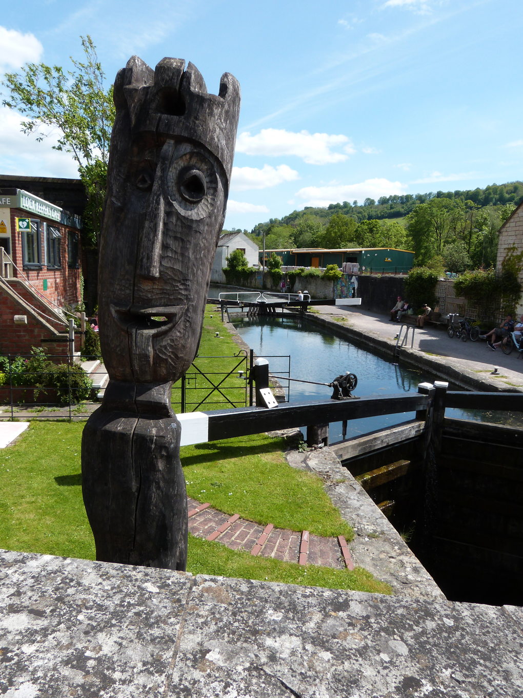 A carved wooden statue overlooks the Wallbridge Upper Lock outside the Lock Keepers Cafe, Stroud. The statue is in the foreground, and the canal and lock recede into the distance.