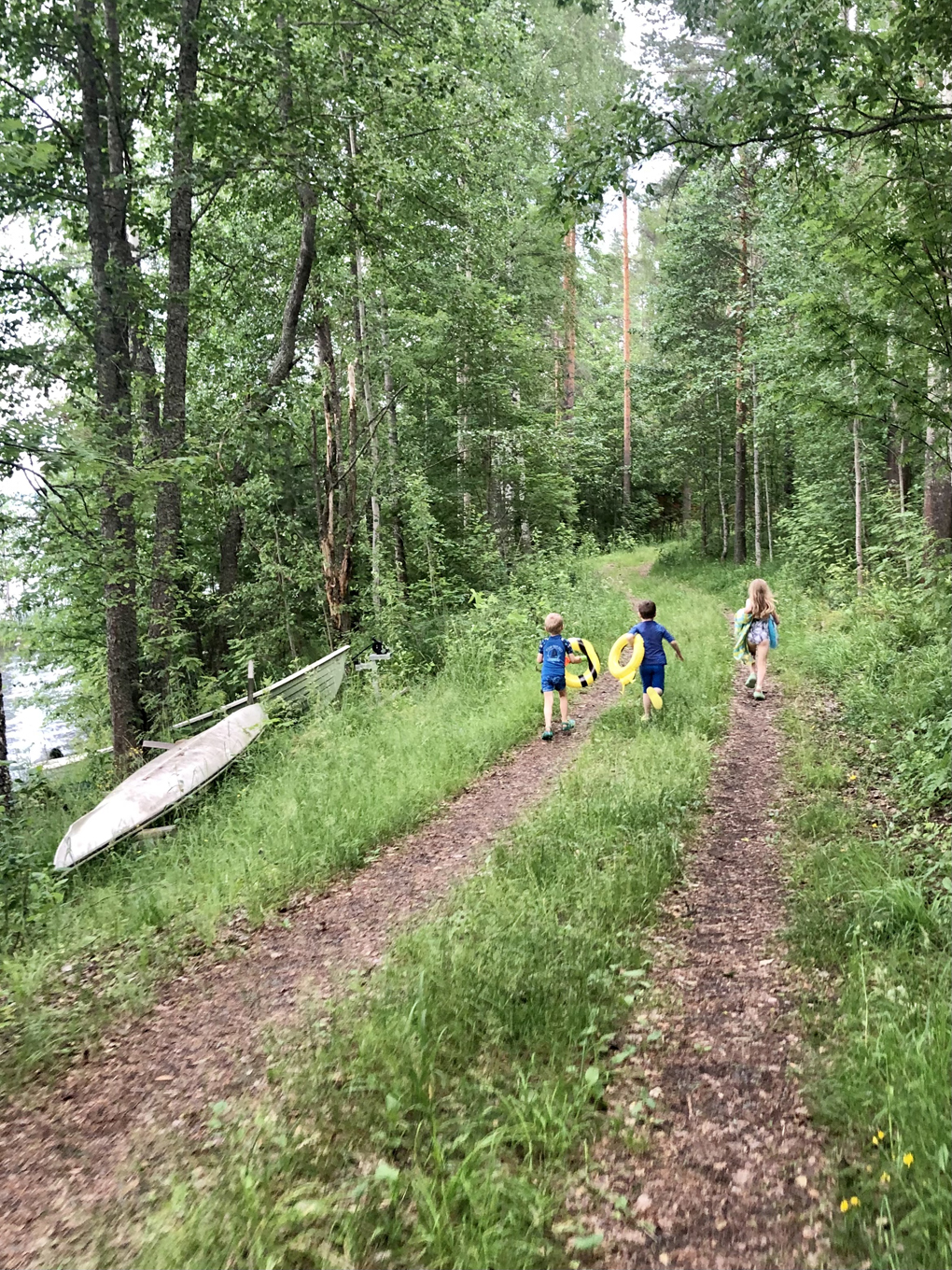 Three children running along a forest road with swimming toys.