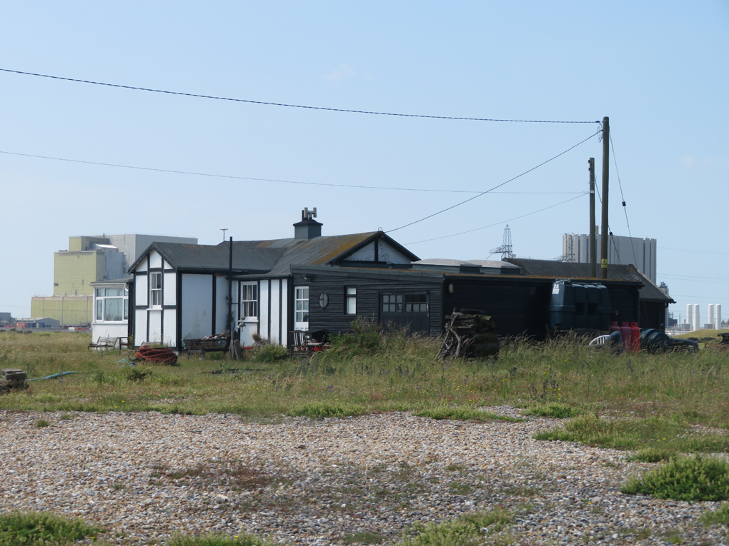 We see the surreal landscape of a Dungeness wooden cabin framed by the nuclear power station