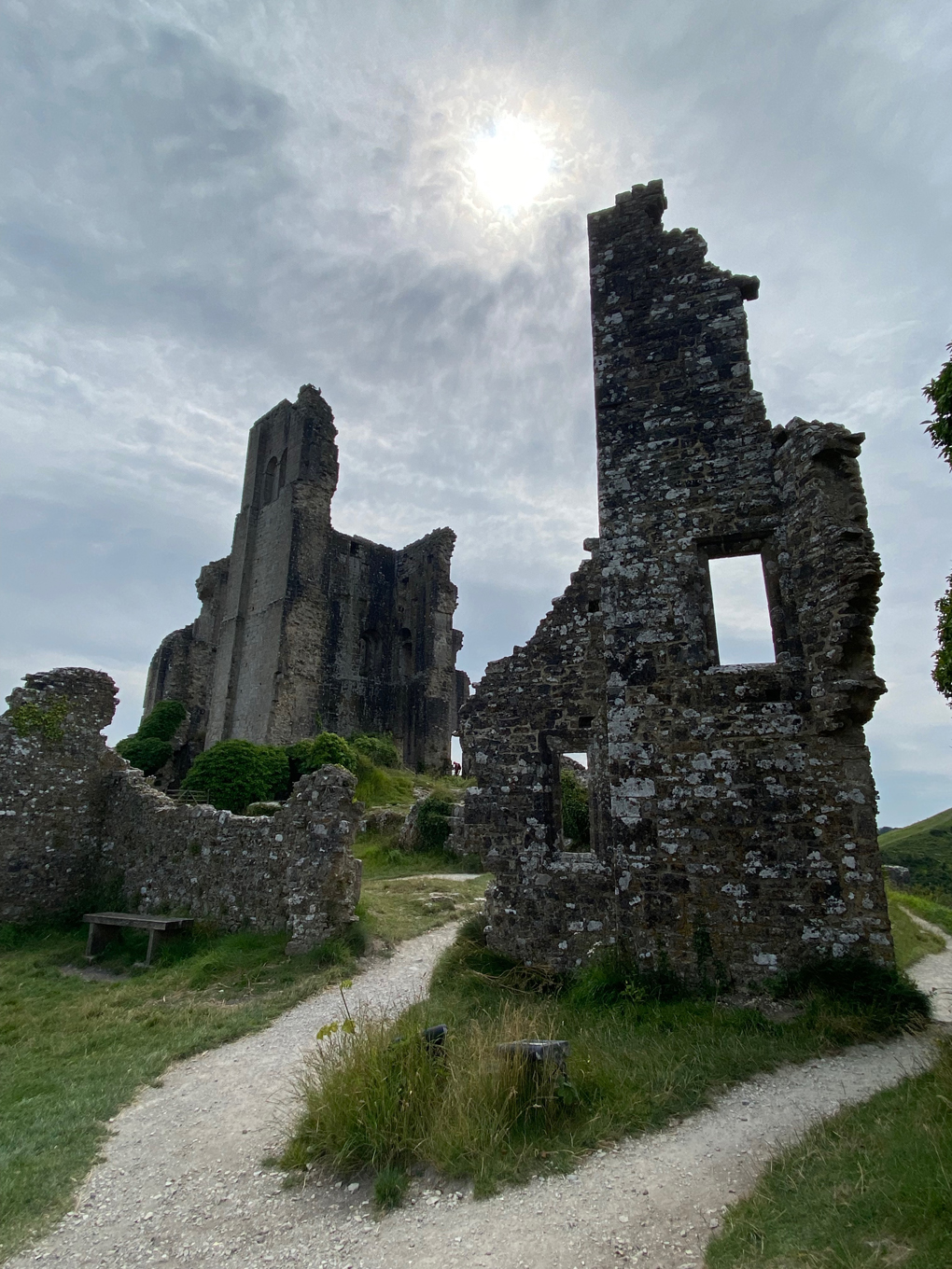 The ruins of Corfe Castle, with the sun breaking through clouds in the background