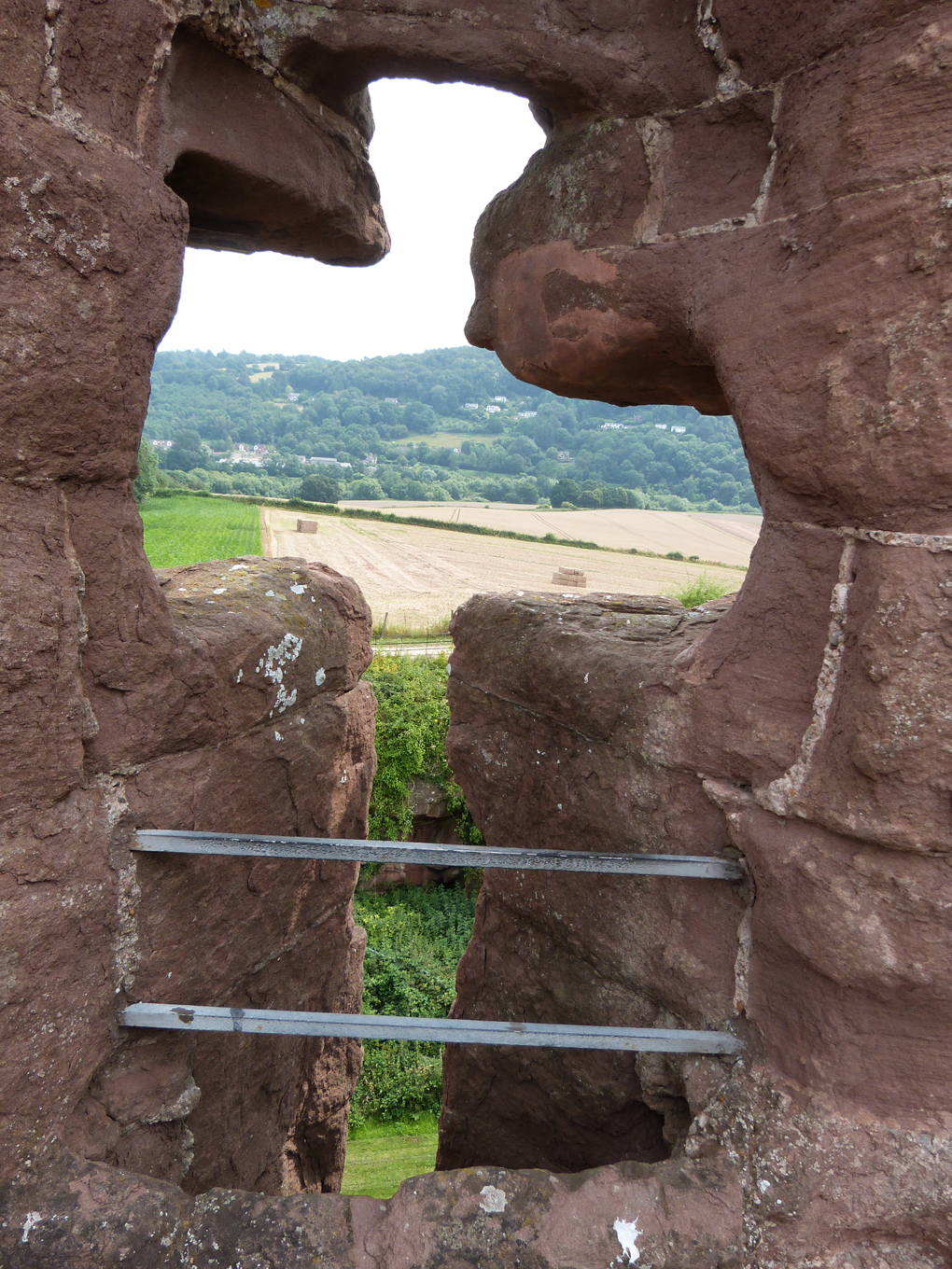 Archer's eye view looking east from Goodrich Castle over the rolling countryside, with the River Wye is in the fold of the hill. The arrowslit or loophole is a narrow vertical opening in the stonework through which the archer can loose his arrow.