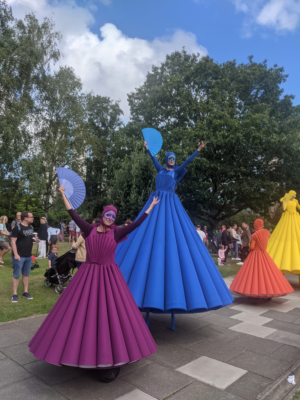 Dancers in long brightly coloured dresses on hoverboards and stilts