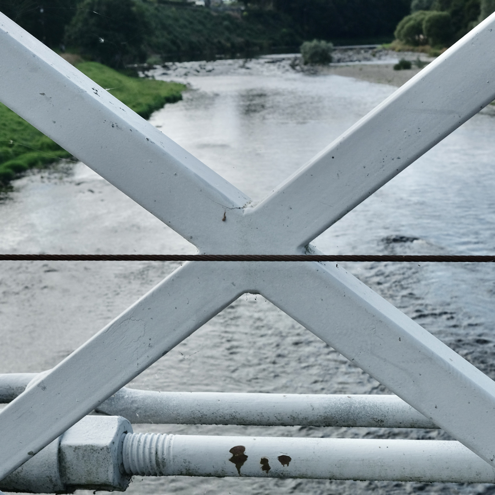 A square photo taken from a bridge over a river. The picture is dominated by a large steel cross, part of the bridge's construction.