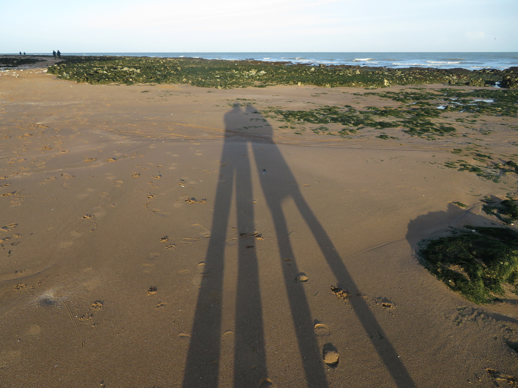 We see two elongated shadows of a couple on the beach, Broadstairs, Kent