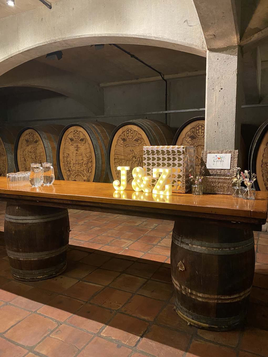An underground wine cellar, with some large barrels in the background. In the foreground there are the letters J and K lit up in lights.