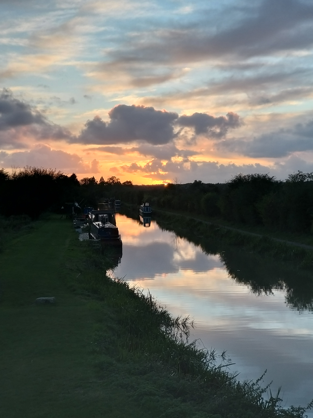 Sunset colours, clouds and hedges reflected in the canal