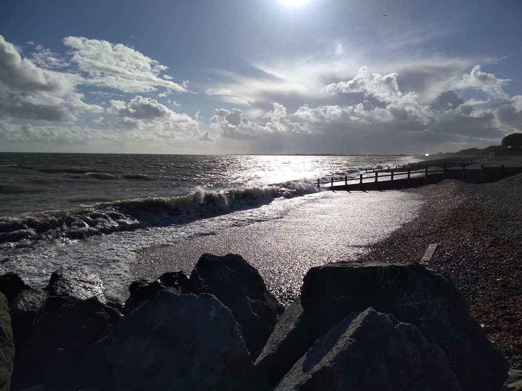 Dark clouds over a rough sea with waves crashing onto a pebble beach and the fading sun reflected on the water