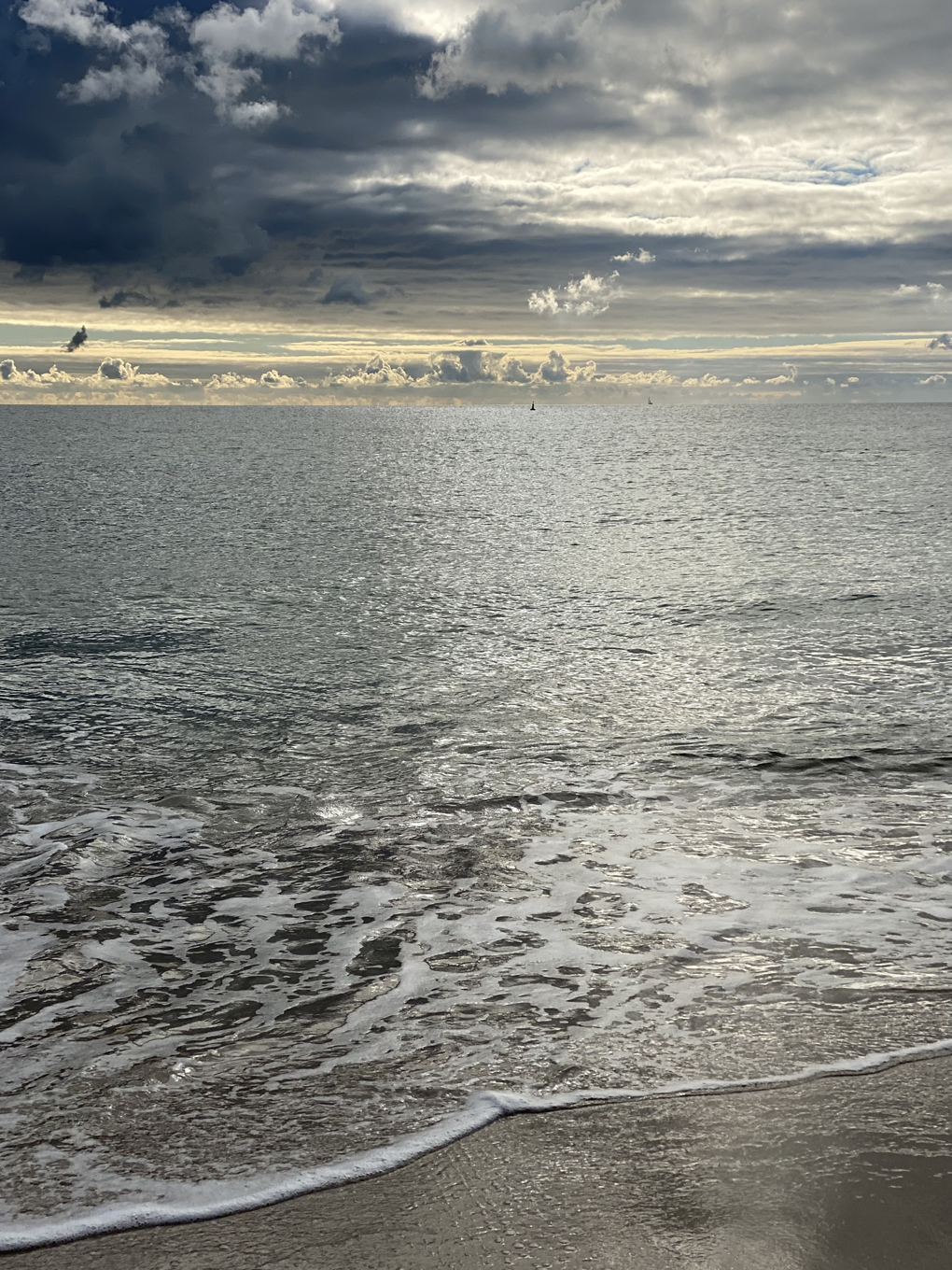 A view of the sea with the beach in the foreground and dramatic clouds in the background