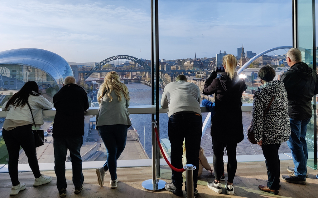 People look out over the Tyne river and bridges from a large glass viewing gallery high in the Baltic Arts Centre