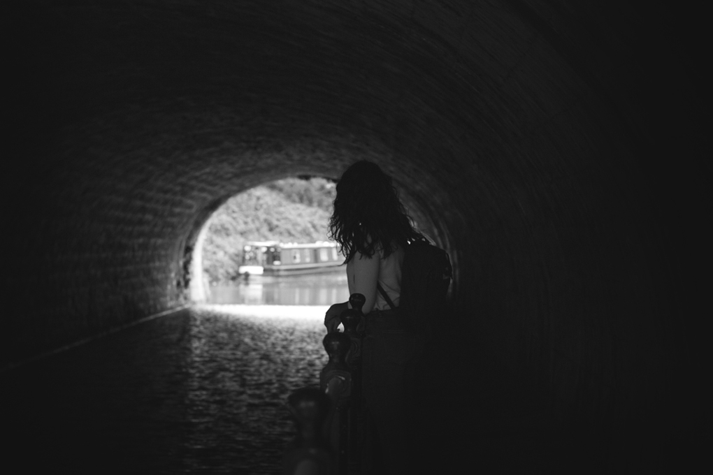 A woman looking towards the end of a dark canal tunnel.