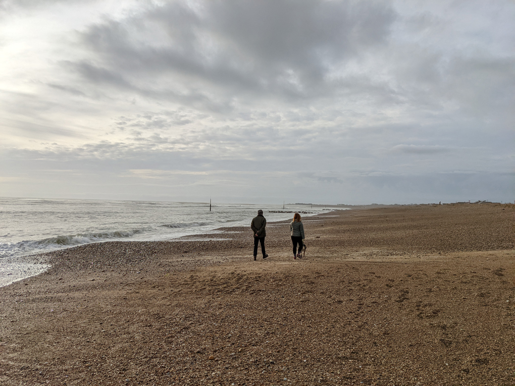 Two people walking along an empty beach together but socially distanced.