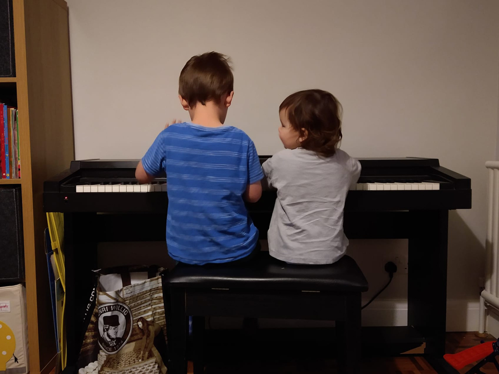 Two children sitting in front of a piano