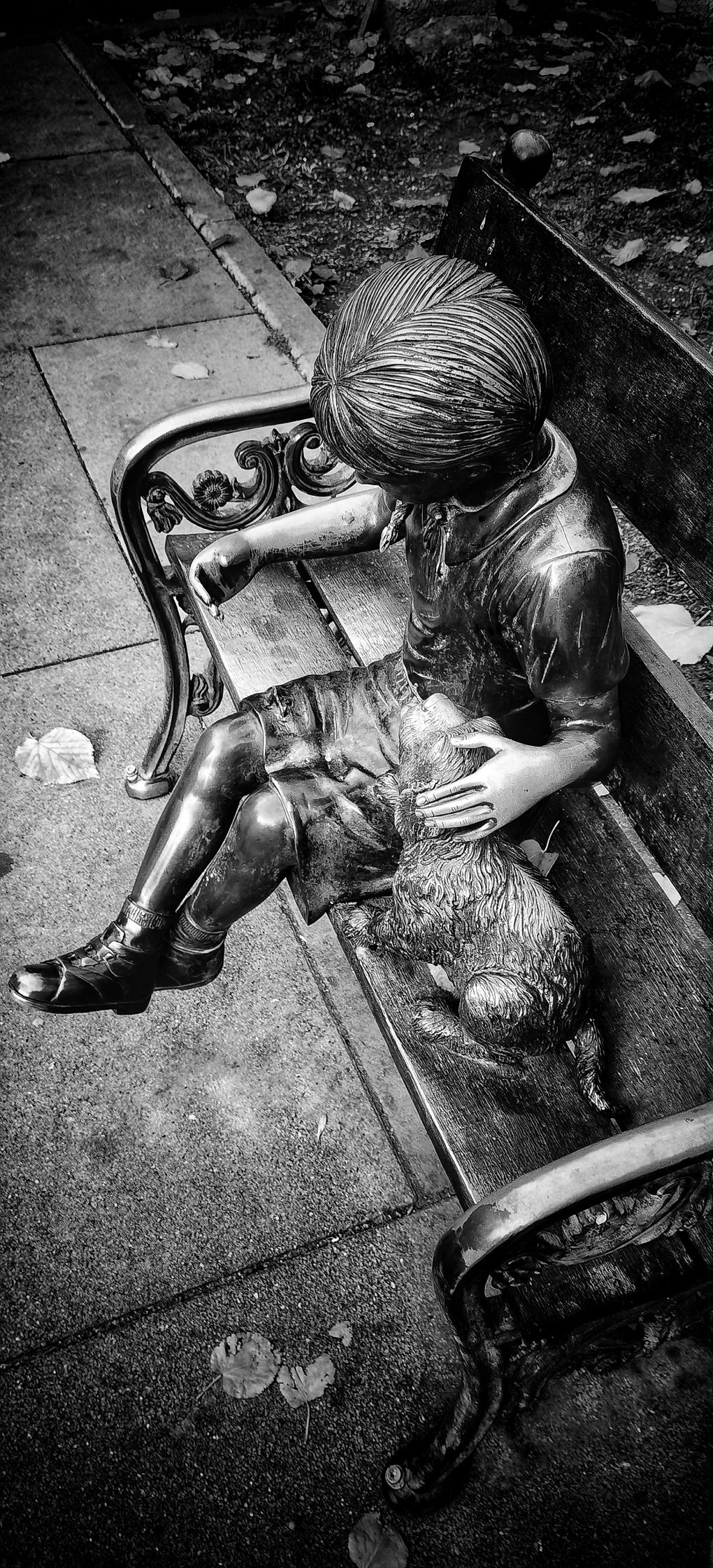 Metal statue of a girl and her dog on a bench.