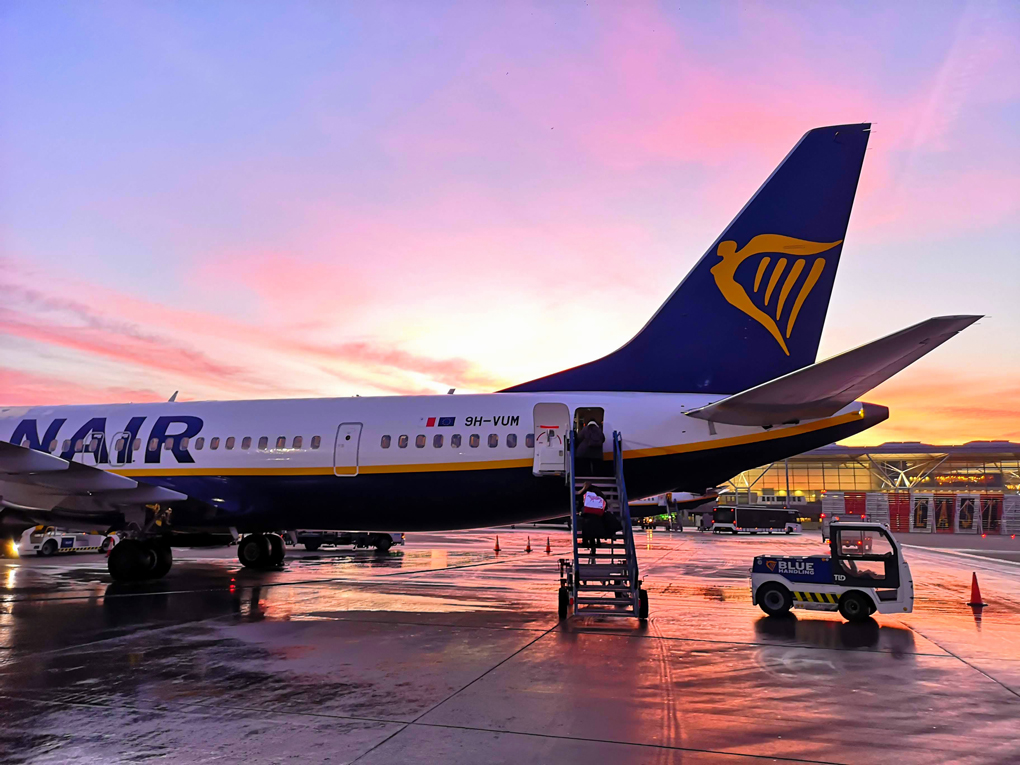 airplane backlit by sunrise and someone walking up the stair to board.