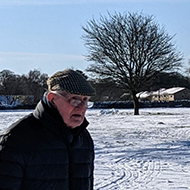 Man walking in snow across a common