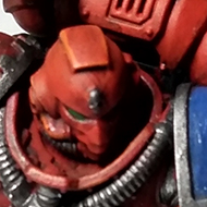 A red armoured space marine miniature sits of a table