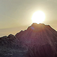 A man stands at the edge of a calm pool of water in the setting sun, his shape reflected in the water below him