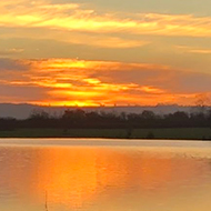 Sunrise over a flooded field, with water flowing from the field across a footpath in the foreground.