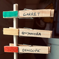 An initiative tracker made from a vertical dowel inserted into a base, with named and coloured clothes pegs for each character