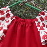 Two red and poppy print girls dresses hanging on tree branches