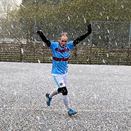 A footballer celebrating a successful shot on goal during a blizzard