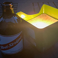 Beer bottle by a lit tea light outside at dusk