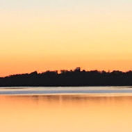 Sun rising in the horizon behind water